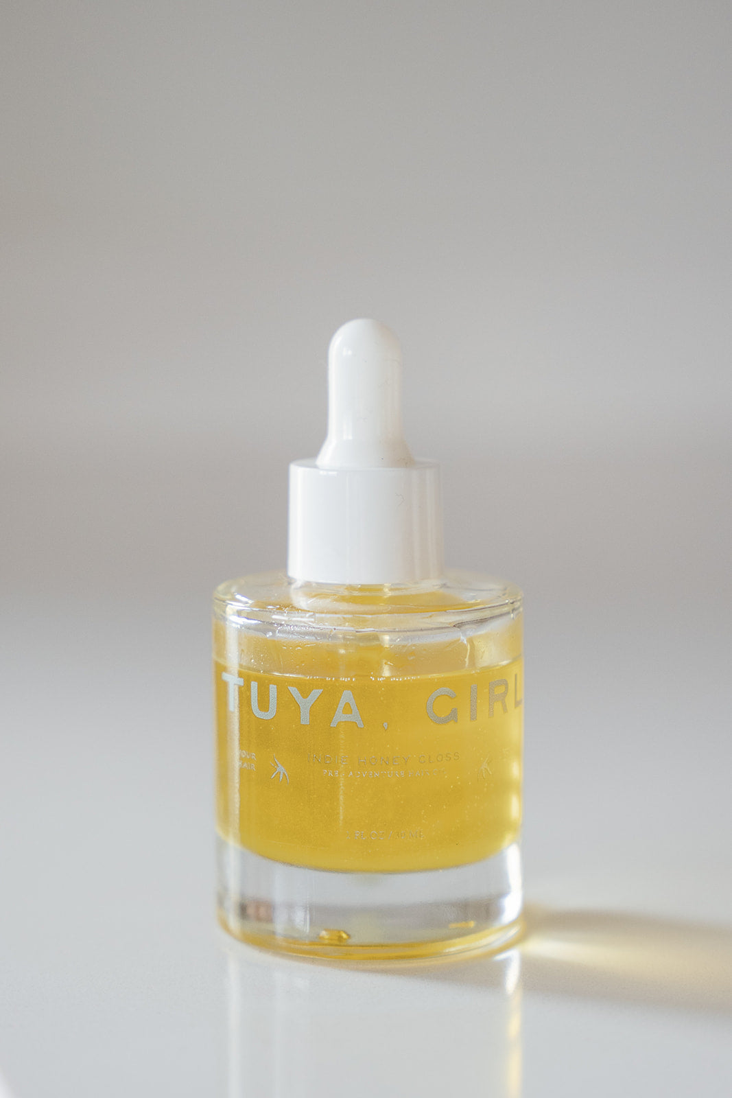 Glass dropper bottle with yellow liquid and white cap on a light gray background